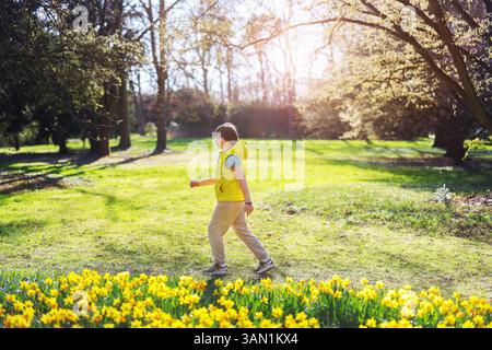 Glücklicher Junge, der auf dem Boden sitzt, umgeben von blühenden weißen Blumen im Frühlingswald Stockfoto