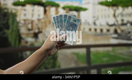 Mann, der polnische Zloty-Banknoten in der Hand hält, auf einer Stadtstraße mit verschwommenem urbanem Hintergrund, was auf Finanzaktivitäten in polen im Freien hindeutet. Stockfoto