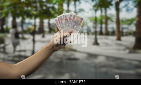 Mann hält polnische Zloty-Banknoten tagsüber auf einer belebten Straße in der Hand und präsentiert eine lebendige Szene des Geldwechsels und des städtischen Lebens Stockfoto
