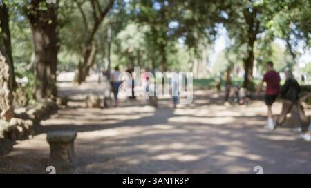 Defokussierte Szene mit Menschen, die durch die Gärten der Villa borghese in rom schlendern, mit verschwommenen Bäumen, einem Pfad und einem Bokeh-Effekt an einem sonnigen Tag. Stockfoto