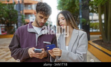 Mann und Frau in lässiger Kleidung mit Telefon und Kreditkarte diskutieren Pläne in einer urbanen Outdoor-Umgebung mit moderner Architektur, die im Hintergrund zu sehen ist Stockfoto