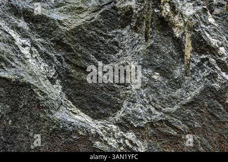 Nahaufnahme einer natürlichen, strukturierten grauen Felsoberfläche mit einzigartigen Mustern und Mineralformationen, die geologische Prozesse im Laufe der Zeit widerspiegeln. Stockfoto