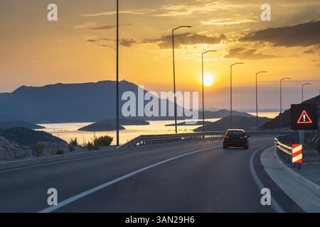 Straße auf der Halbinsel Peljesac in Kroatien, Europa. Panoramastraße bei Sonnenuntergang entlang der Küstenstraße, Berge im Hintergrund. Ein Warnschild weist auf einen Topf hin Stockfoto
