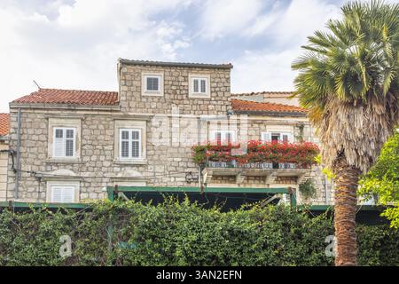 Ston, historische Stadt auf der Halbinsel Peljesac in Kroatien, Europa. Steinhaus mit einem Balkon voller leuchtender roter Blumen unter einem teilweise bewölkten Himmel, kreati Stockfoto