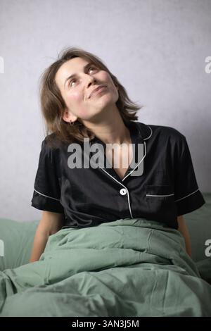 Frau im Bett im schwarzen Satin-Pyjama Stockfoto