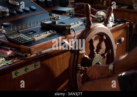 Nahaufnahme des Innenraums eines eleganten Motorbootes. Das hölzerne Lenkrad und die Motorsteuerung sind ebenso zu sehen wie die Hand des Kapitäns. Stockfoto