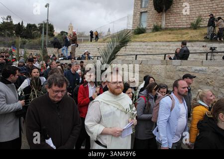 Christliche Pilger in der ganzen Welt singen und beten, während sie auf dem Mt. Oliven in einer Palmensonntagsprozession mit Palmenwedel und Olivenbaumzweigen. Stockfoto