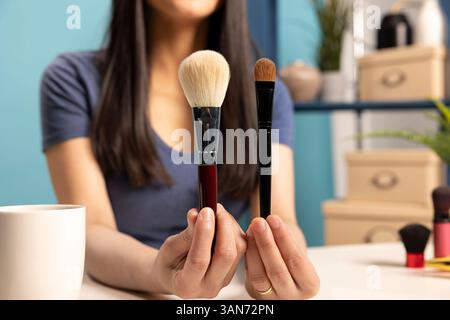 Nahaufnahme eines Influencers für soziale Medien, der zwei Make-up-Pinsel präsentiert und sie für eine detaillierte Ansicht nahe an der Kamera hält. Schönheitsvlogger, der Inhalte über Kosmetikgeräte für das Schminken erstellt. Stockfoto