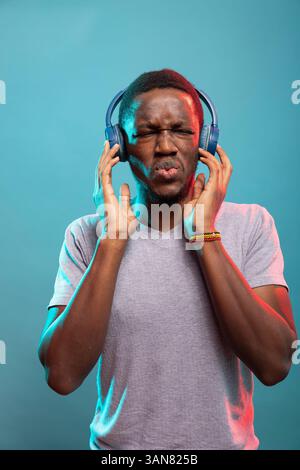 Männlicher Influencer mit schnurlosem Headset, der schöne Geräusche genießt und den Rhythmus spürt. Schwarzer Mann mit Kopfhörern, eingetaucht in sein Lieblingslied, lauscht vor isoliertem Hintergrund. Stockfoto