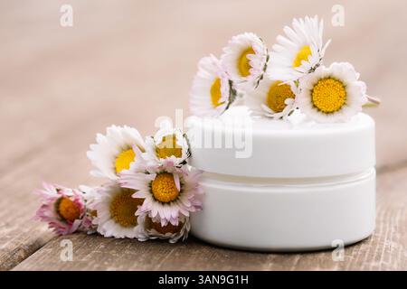 Nahaufnahme von Kollagencreme im Glasgefäß mit Gänseblümchen auf Holzoberfläche Stockfoto