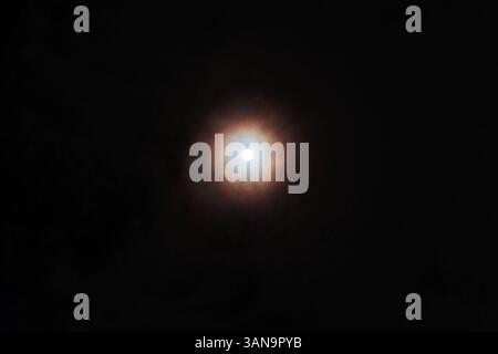 Heller Vollmond, der mit einem bunten Halos am dunklen, bewölkten Nachthimmel leuchtet. Stockfoto