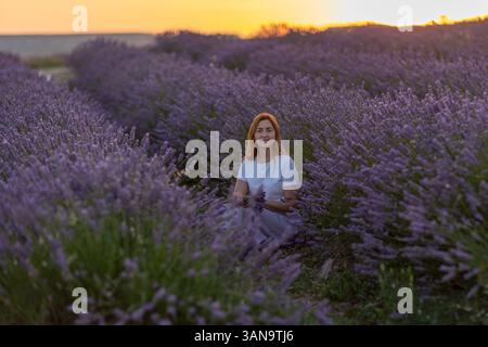 Eine Frau sitzt auf einem Feld mit Lavendelblumen Stockfoto