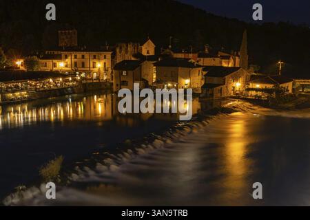 Stimmungsvolle Nachtaufnahme eines beleuchteten Dorfes am Fluss mit reflektierenden Lichtern, Valeggio sul Mincio, Borghetto, Provinz Verona in Veneto, IT Stockfoto