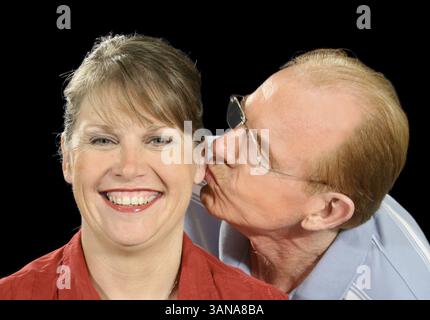 Ein Mann mittleren Alters gibt seiner Frau einen Peck aufs Ohr Stockfoto