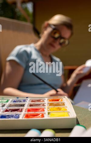 Aquarellfarben, Pinsel liegen auf dem Tisch vor dem Hintergrund eines verschwommenen Künstlers Stockfoto