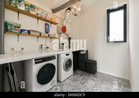 Ein moderner Waschraum mit sauberem und organisiertem Raum mit Waschmaschinen, Regalen und stilvollen Dekorationselementen. Eine perfekte Mischung aus Funktionalität und Ästhetik. Stockfoto