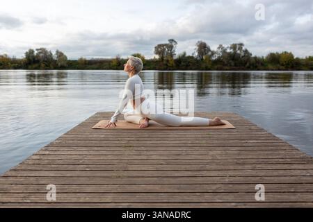 Reife Frau, die Yoga übt, Übungen an vier Gliedmaßen macht, Liegestütze vom Boden, halbe Pose der Königstaube, Eka Pada Rajakapotasana, Training Stockfoto