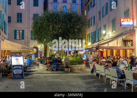Die Gäste speisen in Cafés und Restaurants im Freien auf dem kleinen abendlichen Stadtplatz in Menton, der Stadt an der französischen Riviera. Stockfoto