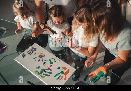 Die Familie versammelt sich um einen Tisch, um kreative Fingermalerei zu betreiben. Kinder verwenden fröhlich ihre Hände, um farbenfrohe Drucke auf Leinwand zu kreieren, die zum Ausdruck bringen Stockfoto