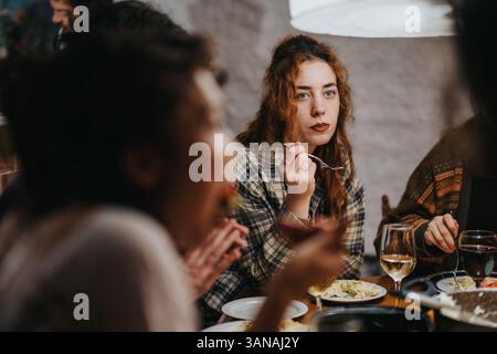 Gruppe von Freunden, die gemeinsam an einem gemütlichen Tisch bei schwacher Beleuchtung zu Abend essen Stockfoto