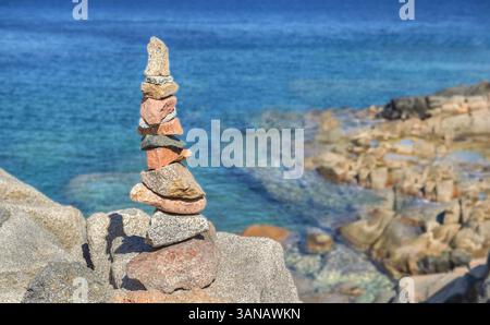 Rote und graue Kieselsteine stapeln sich auf dem Felsen vor dem wunderschönen Meer der Insel Sardinien Stockfoto