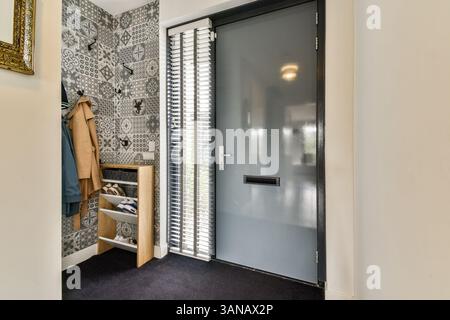 Ein moderner Eingang mit einer eleganten Tür, gemusterten Wänden und organisierter Ablage. Das stilvolle Dekor unterstreicht das gesamte Ambiente des Raumes. Stockfoto