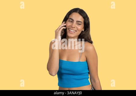 Glückliche junge Frau spricht auf dem Smartphone und lächelt auf gelbem Hintergrund Stockfoto