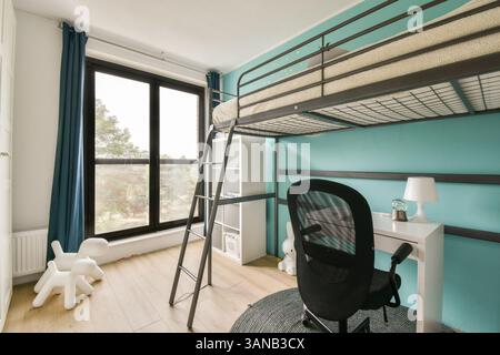 Ein lebhaftes, modernes Schlafzimmer mit Loft-Bett, Schreibtisch und Blick durch große Fenster, die durch türkisfarbene Wände und minimalistische Einrichtung unterstrichen werden. Stockfoto