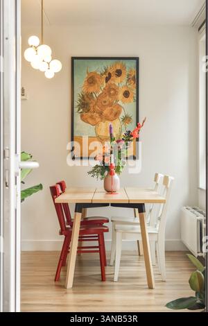 Ein moderner Speisesaal mit einem einzigartigen Tisch, roten und weißen Stühlen und leuchtenden Sonnenblumenkunstwerken an der Wand. Die Atmosphäre ist frisch und einladend. Stockfoto