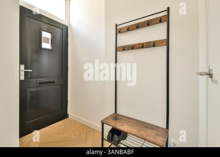 Ein eleganter und moderner Eingangsbereich mit schwarzer Tür, Holzgarderobe und elegantem Fußboden mit modernen Designelementen. Stockfoto