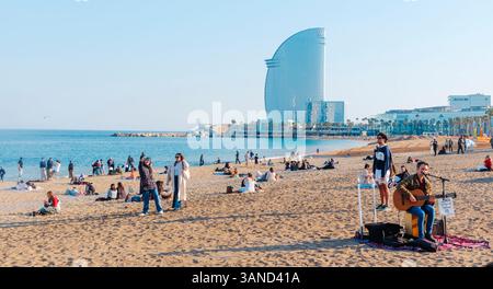 Barcelona, Spanien - 28. März 2025: Menschen am Strand von Sant Sebastia in Barcelona, Spanien, an einem Frühlingstag, und das W Barcelona Hotel, das bei Einheimischen beliebt ist Stockfoto