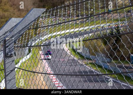 Blick durch einen Sicherheitszaun auf die Rennstrecke Nürburgring. Verschwommene Racing-Action im Hintergrund. Motorsport-Sicherheit. Stockfoto