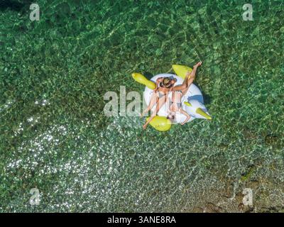 Luftaufnahme zweier Frauen in Bikinis auf aufblasbarer Tiermatratze in Panagopoula, Griechenland. Stockfoto