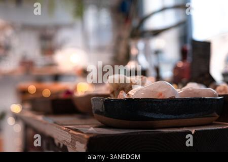 Eine flache, dunkle Keramikschale gefüllt mit verschiedenen rauen Edelsteinen sitzt auf einem rustikalen Holzregal mit verschwommenem Hintergrund Stockfoto