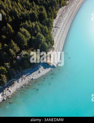 Blick aus der Vogelperspektive auf immergrüne Bäume und türkisblaues Gletscherwasser am Rande des Lake Pukaki, Südinsel, Neuseeland Stockfoto