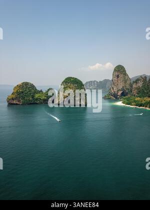 Aus der Vogelperspektive winzige Schnellboote erkunden die riesigen Kalksteinklippen und Inseln im türkisblauen Meer, einem tropischen Paradies, Phra Nang, Krabi, Phu Stockfoto