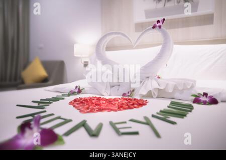 Schwäne aus Handtüchern sind ein Symbol für Liebe und Beziehungen, und ein Herz aus Rosenblüten auf einem weißen Bett für Liebhaber in einem Hotelzimmer aus nächster Nähe. Th Stockfoto