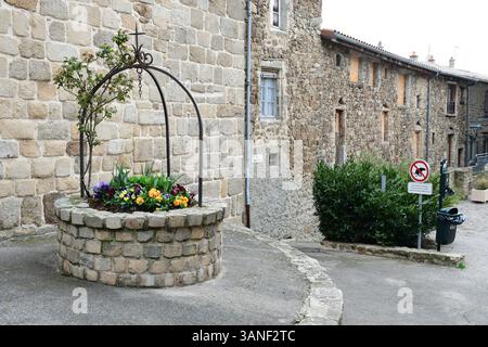 Blumendekoration mit Stiefmütterchenblumen vor der Kirche des mittelalterlichen Dorfes. Ein mittelalterliches Dorf in Frankreich bietet einen Einblick in das Leben vor Jahrhunderten, mit engen kopfsteingepflasterten Gassen, Steinhäusern und Fachwerkhäusern, die oft um eine zentrale Kirche oder Burg gruppiert sind. Diese Dörfer waren autarke Gemeinden, in denen die Menschen bewirtschafteten, auf Märkten gehandelt und im Rhythmus der Jahreszeiten lebten. Umgeben von Schutzmauern oder hoch auf Hügeln zur Verteidigung, haben viele ihren ursprünglichen Charme und ihre Architektur erhalten und sind heute bei Geschichtsliebhabern und Touristen beliebt. Stockfoto