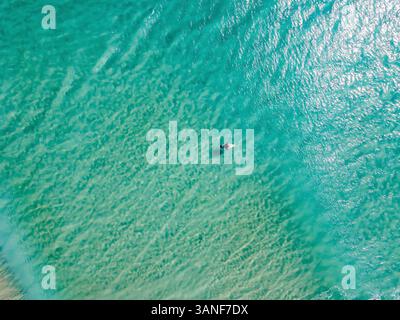 Drohnenansicht eines Surfers auf seinem Board am Pass in der Nähe von Byron Bay in New South Wales, Australien. Das Wasser ist durchsichtig und die Sonne reflektiert sich Stockfoto