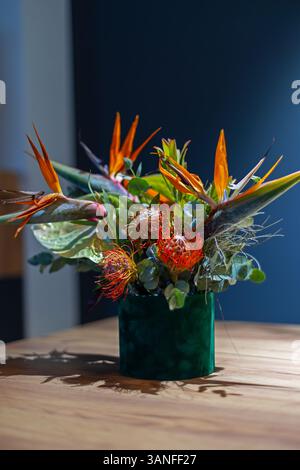 Exotisches Blumenarrangement mit Paradiesvogel und Protea-Blüten in einer grünen Vase. Stockfoto