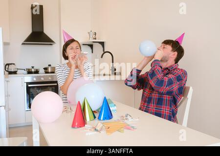 Das junge Paar feiert zu Hause gemütlich Geburtstag und genießt Kuchen und Lachen in warmer Atmosphäre. Fröhliche Atmosphäre, farbenfrohe Dekoration, Vorbereitung auf die Feiertagsparty, Dekoration Küchenraum Stockfoto