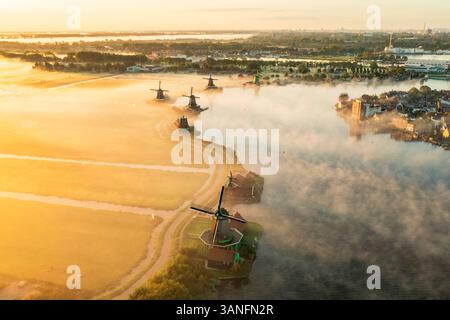 Blick aus der Vogelperspektive auf traditionelle Windmühlen im Nebel bei Sonnenaufgang, Zaanse Schans, Niederlande. Stockfoto