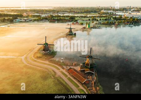 Blick aus der Vogelperspektive auf traditionelle Windmühlen im Nebel bei Sonnenaufgang, Zaanse Schans, Niederlande. Stockfoto