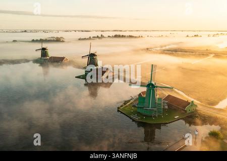 Blick aus der Vogelperspektive auf traditionelle Windmühlen im Nebel bei Sonnenaufgang, Zaanse Schans, Niederlande. Stockfoto