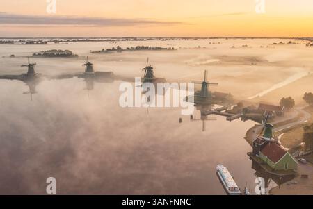 Blick aus der Vogelperspektive auf traditionelle Windmühlen im Nebel bei Sonnenaufgang, Zaanse Schans, Niederlande. Stockfoto