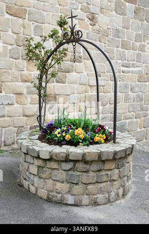 27. März 2025, Boulieu Les Annonay, Ardeche, Frankreich: Blumendekoration mit Stiefmütterchen vor der Kirche des mittelalterlichen Dorfes. Ein mittelalterliches Dorf in Frankreich bietet einen Einblick in das Leben vor Jahrhunderten, mit engen kopfsteingepflasterten Gassen, Steinhäusern und Fachwerkhäusern, die oft um eine zentrale Kirche oder Burg gruppiert sind. Diese Dörfer waren autarke Gemeinden, in denen die Menschen bewirtschafteten, auf Märkten gehandelt und im Rhythmus der Jahreszeiten lebten. Umgeben von Schutzmauern oder auf Hügeln zur Verteidigung, erhalten viele ihren ursprünglichen Charme und ihre Architektur Stockfoto