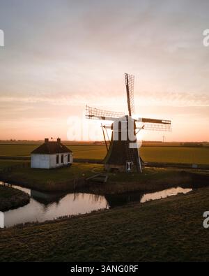 Aus der Vogelperspektive auf eine malerische Windmühle bei Sonnenaufgang mit ruhigen Reflexen auf dem Wasser, Tjerkwerd, Niederlande. Stockfoto