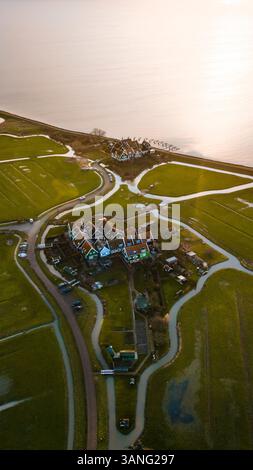Blick aus der Vogelperspektive auf ein malerisches Dorf mit traditionellen Häusern an einem ruhigen See bei Sonnenaufgang, Marken, Nord-Holland, Niederlande. Stockfoto