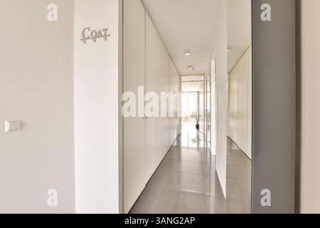 Ein eleganter, moderner Flur mit weißen Wänden und minimalistischen Designelementen führt zu einem hellen und geräumigen Wohnbereich mit Tageslicht. Stockfoto