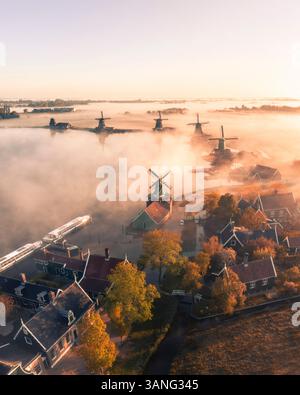 Blick aus der Vogelperspektive auf traditionelle Windmühlen im Nebel bei Sonnenaufgang, Zaanse Schans, Niederlande. Stockfoto